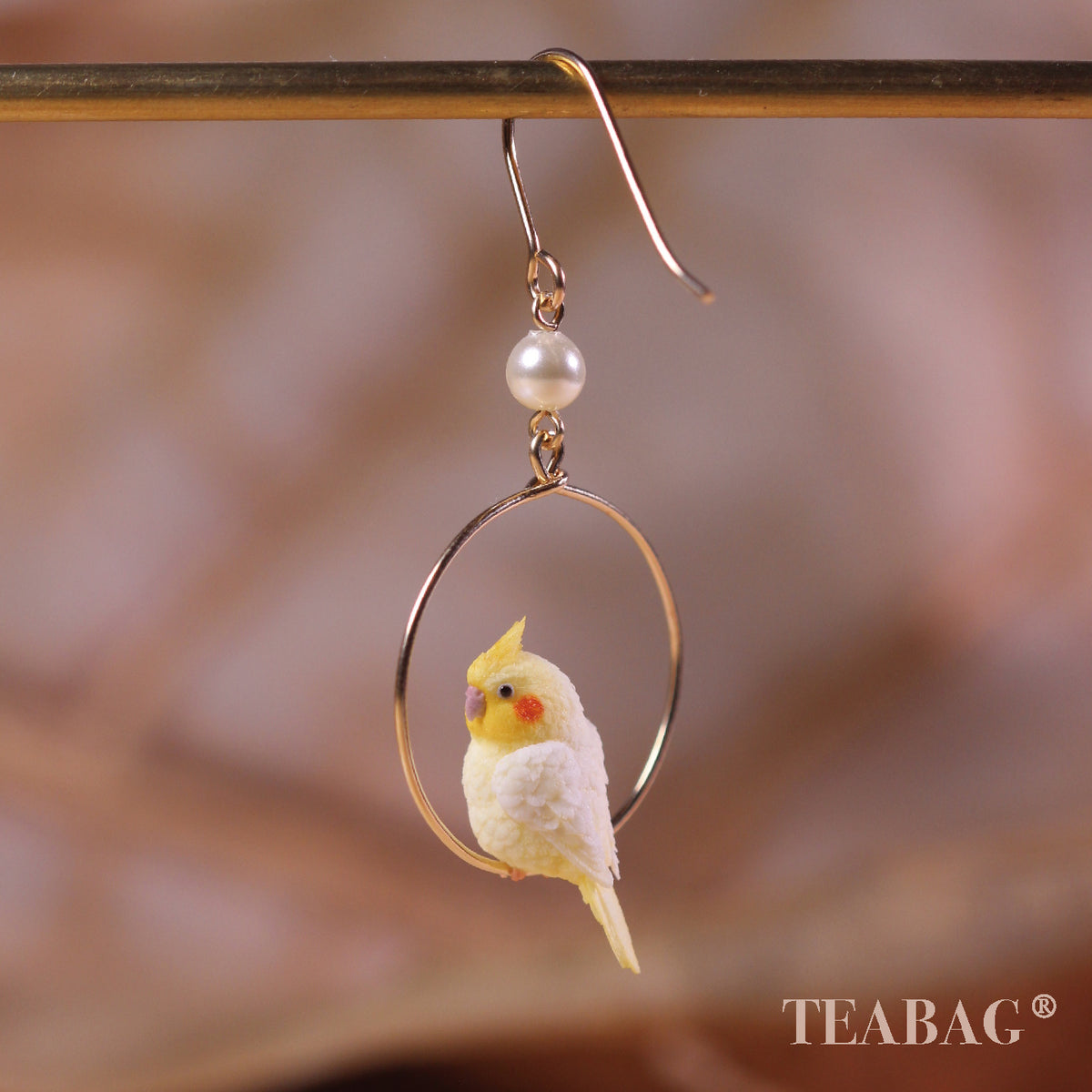 Side view of one cockatiel hoop earring, showing the full pierced hook, white pearl and bird tail.