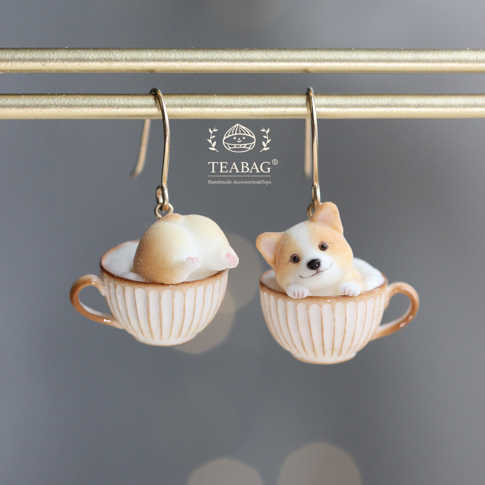 Pair of Corgi Coffee hook earrings, with one front-facing corgi and one rear-view corgi in cream-and-gold cups, showing the complete hooks and TEABAG branding.