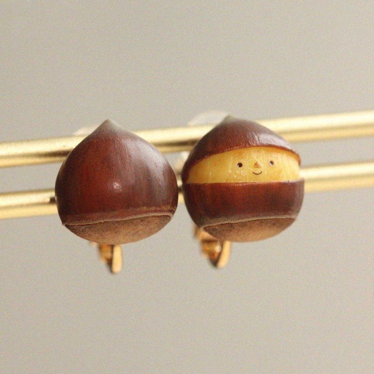 Square front-and-back view of the smiling chestnut clip-on earrings on gold-colored display rods, with both complete clip fittings visible.