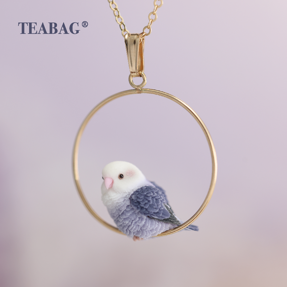 Violet lovebird pendant seen from the front, with a complete round hoop, bail and chain section, showing its pale face and layered purple wings.