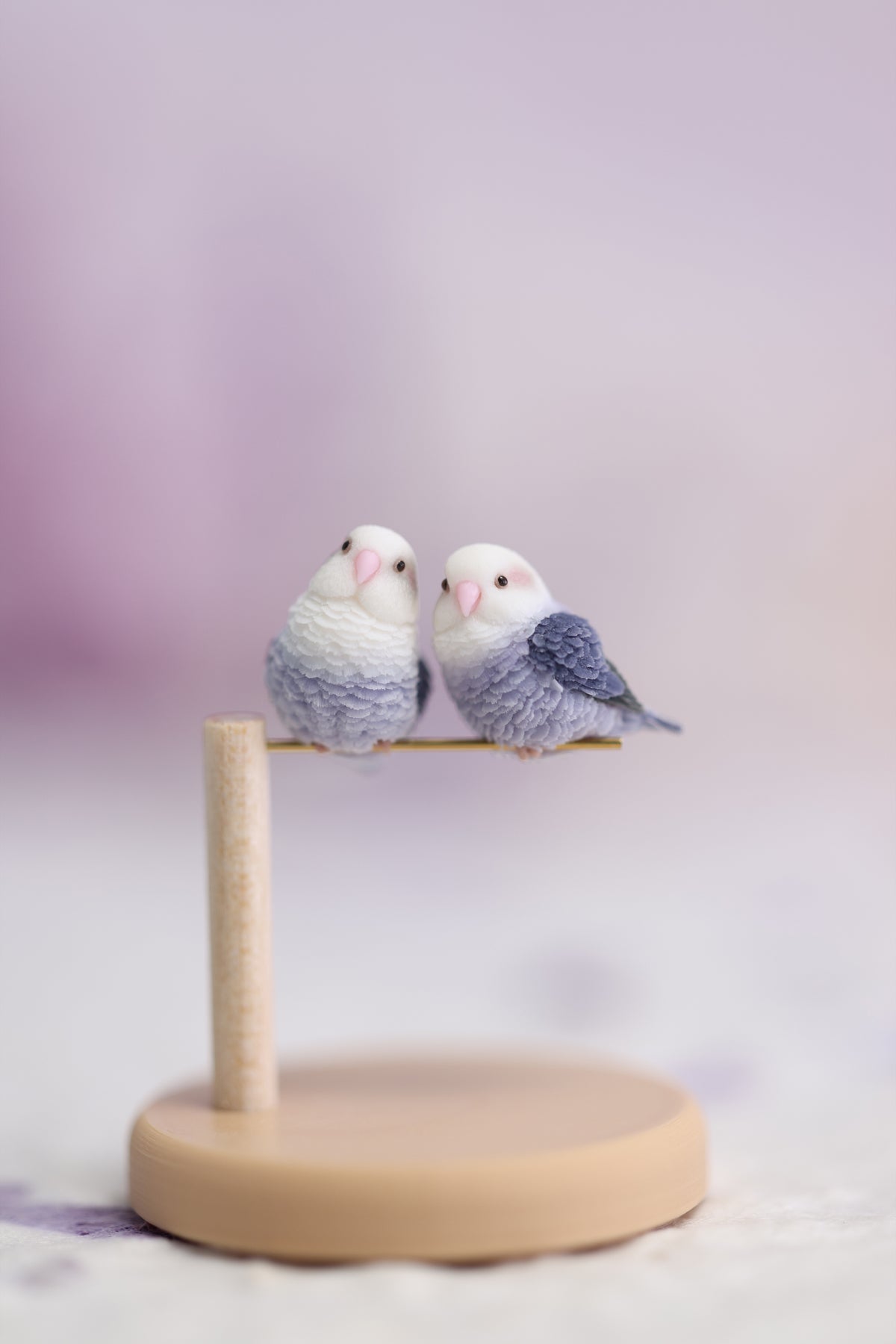 Two violet lovebird miniatures, one tilted-head and one side-facing, together on one complete display stand with a pine post and round base.