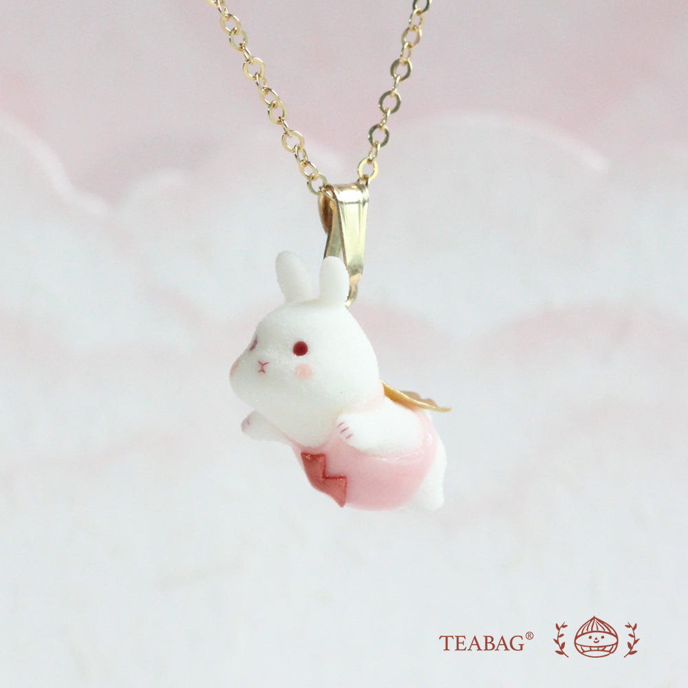 White flying-bunny pendant in pink with its complete bail and chain against a soft pink background, with TEABAG branding.