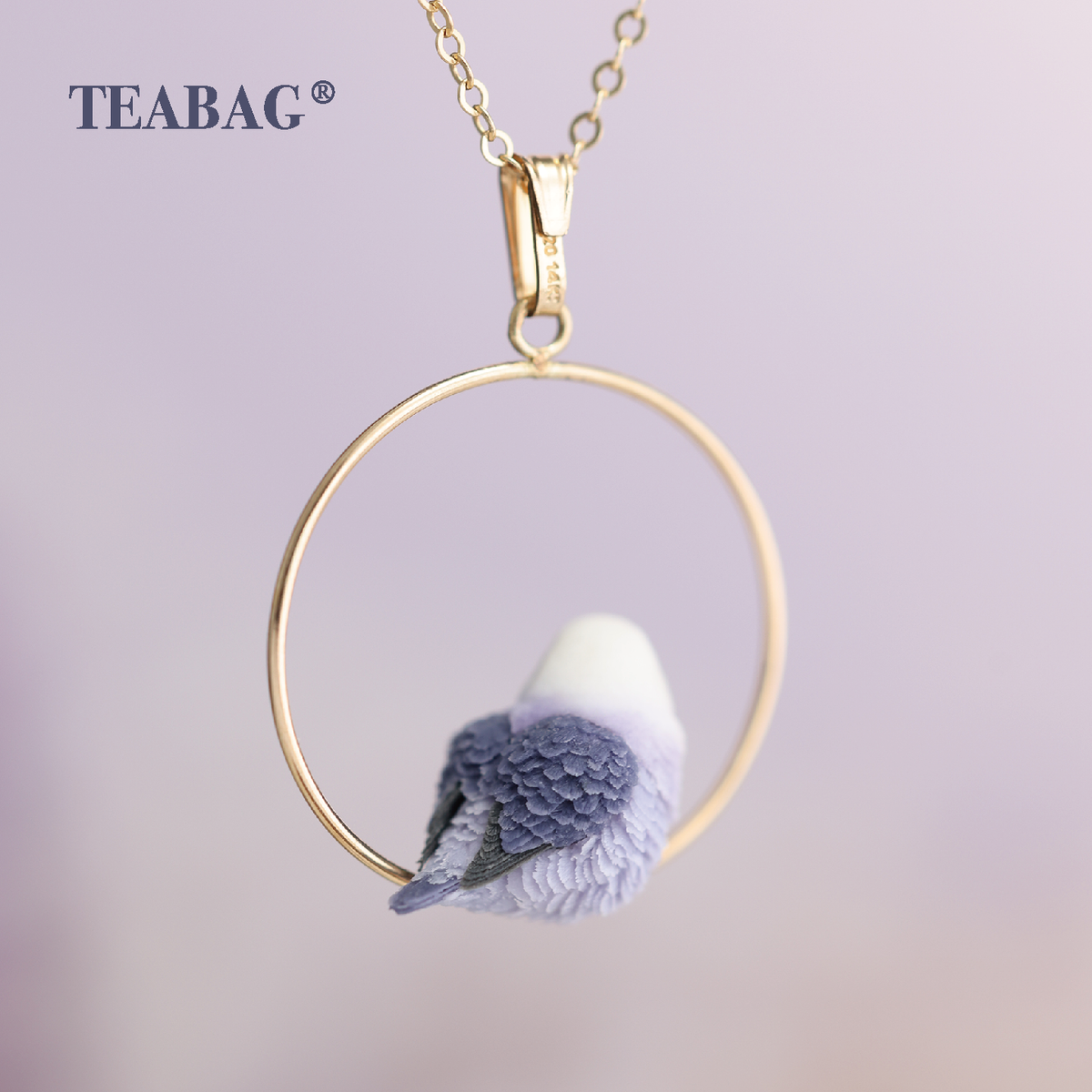 Rear view of the violet lovebird pendant, showing its layered purple wings, tail, complete hoop and bail with a chain section.