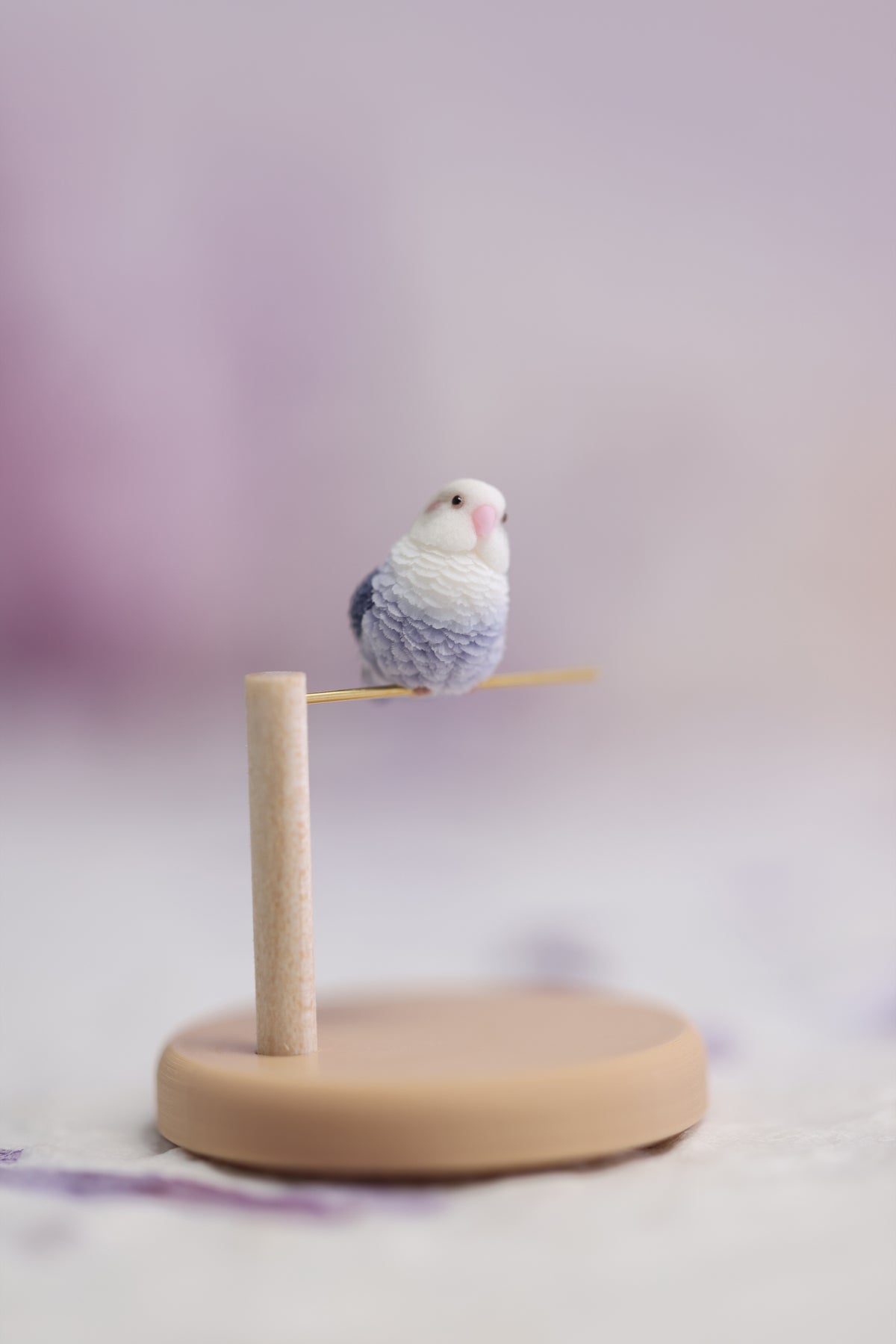One tilted-head violet lovebird miniature on a complete display stand, showing the full pine post, gold-tone perch and round base.