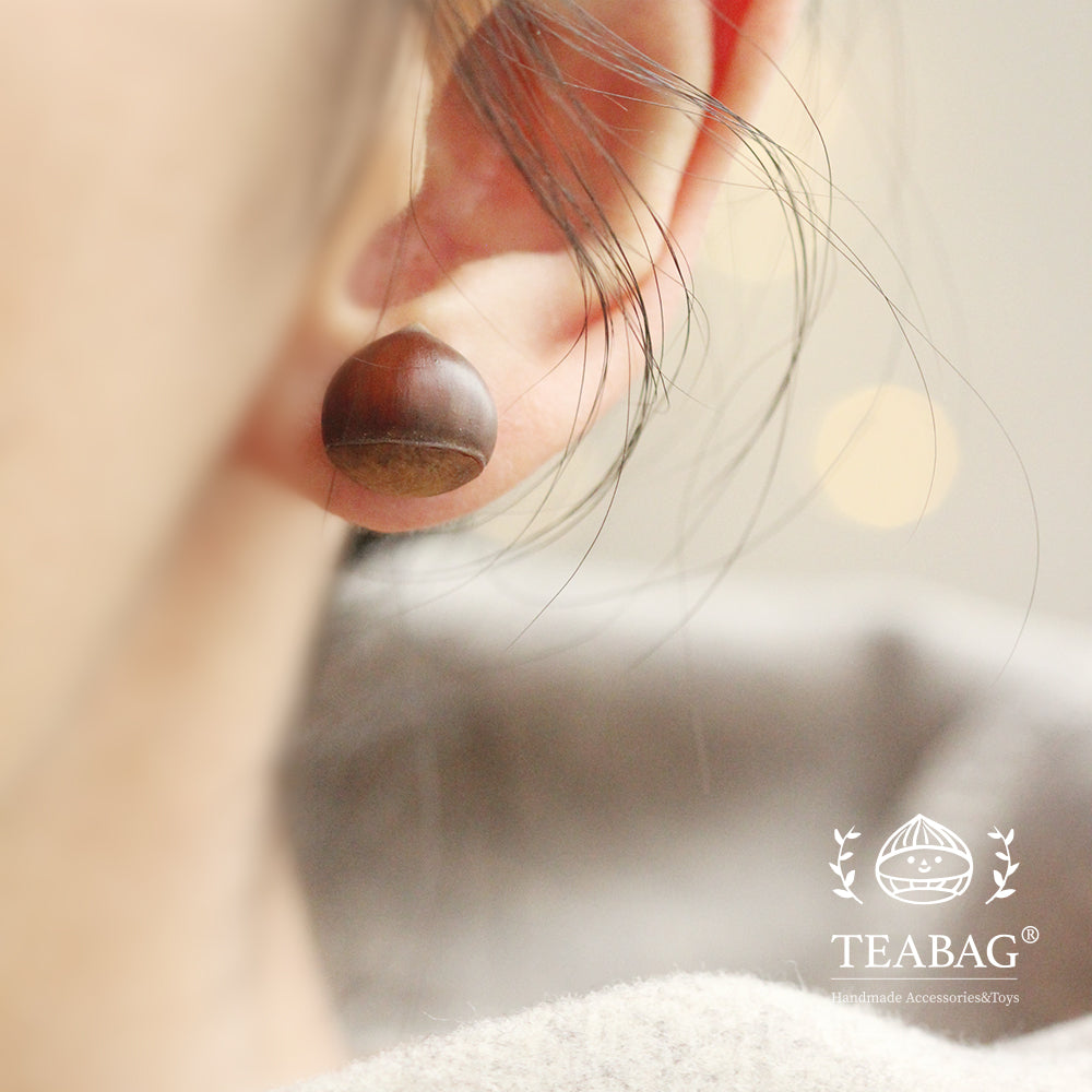 Chestnut earring worn on an earlobe, showing its rounded brown back.
