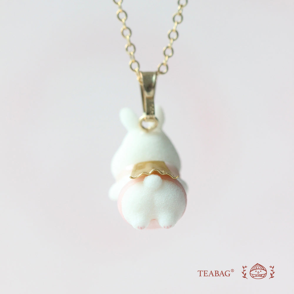 Rear view of the flying-bunny pendant showing the gold-colored cape, white tail, bail and chain, with TEABAG branding.