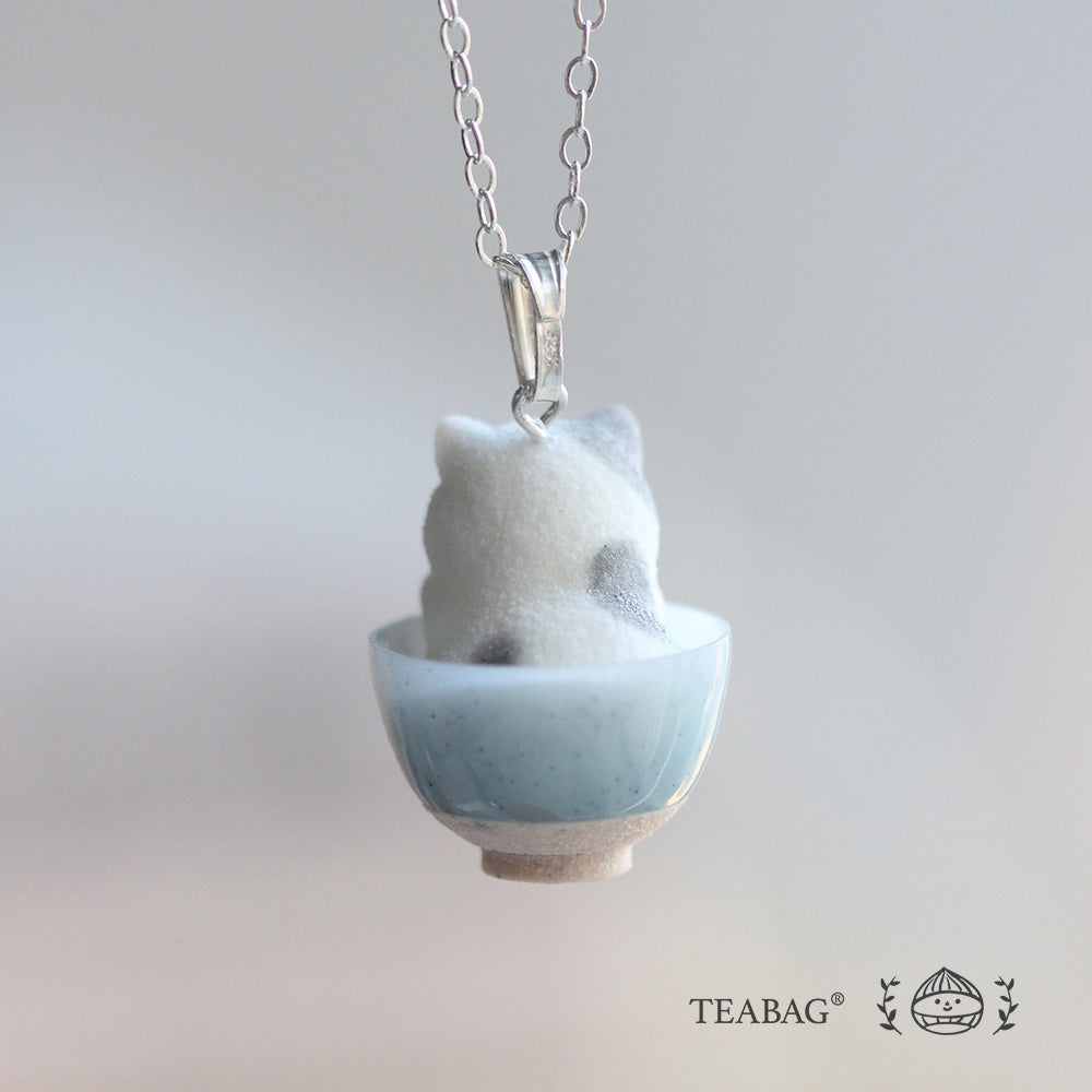 Rear view of the Kitten Bakery necklace, showing the kitten in its blue bowl, the bail and a section of chain. TEABAG logo.