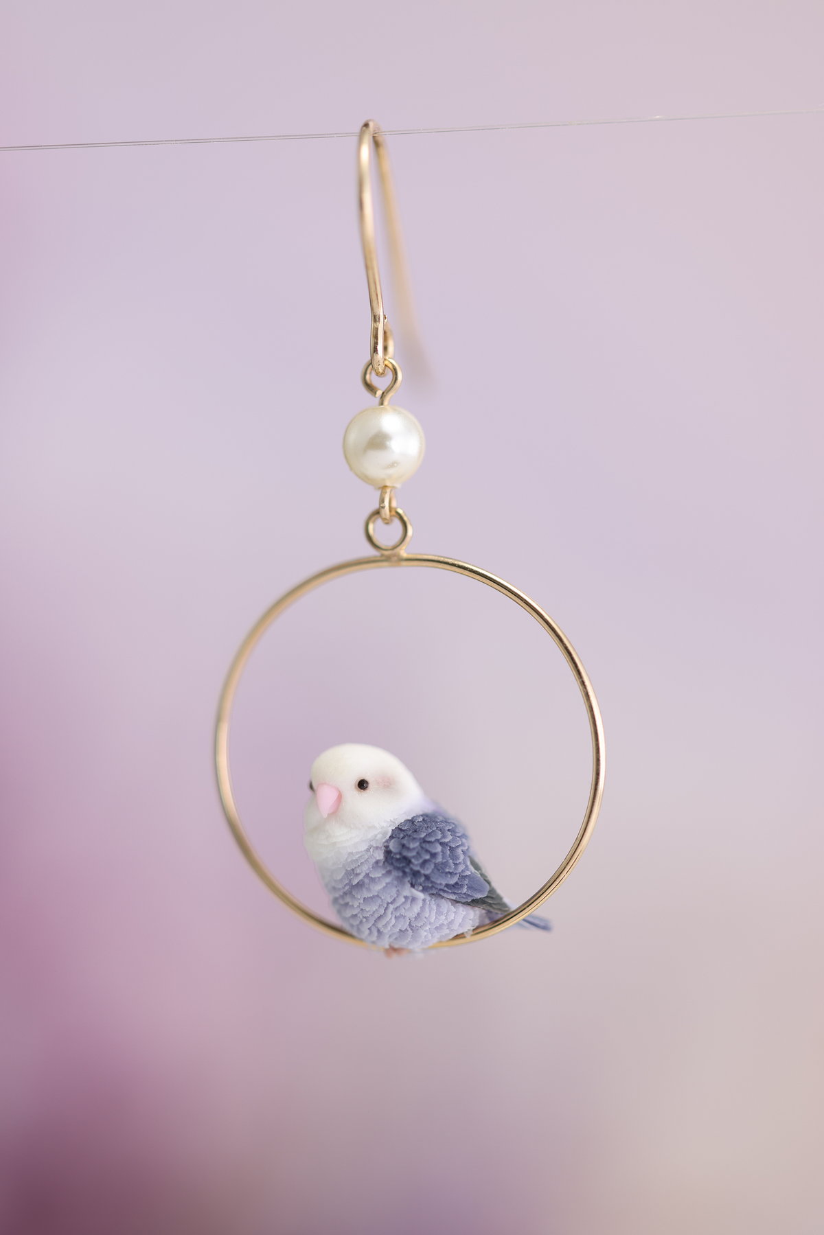 Single side-facing violet lovebird earring showing the complete pierced hook, white bead, hoop and sculpted feathers. Sold as a pair.