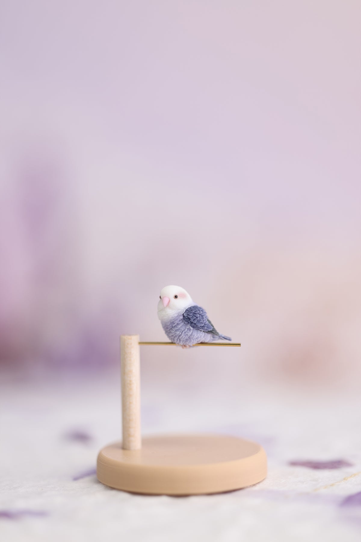 One side-facing violet lovebird miniature on a complete display stand, showing the full pine post, gold-tone perch and round base.
