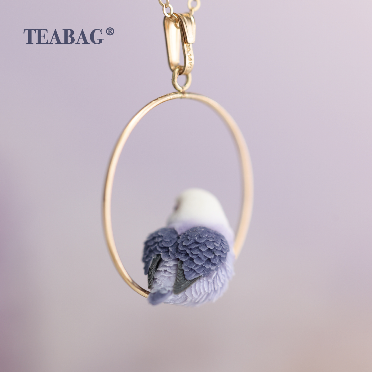 Rear view of the Violet Lovebird Necklace, showing layered purple wings and tail inside the gold-colored hoop, with bail, chain section and TEABAG branding.