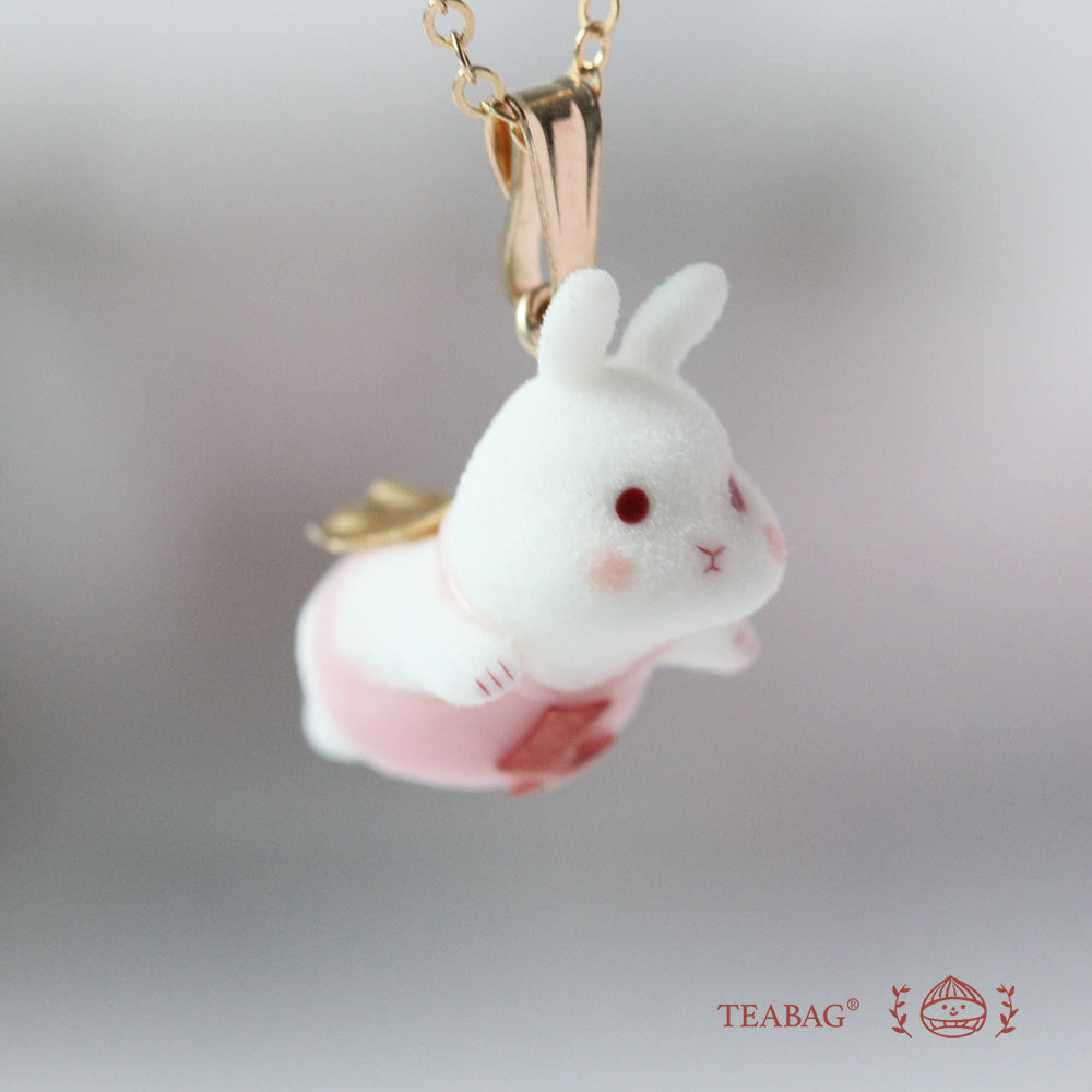 Close-up of the white flying-bunny pendant with pink clothing, red eyes, cape, bail and chain, with TEABAG branding.