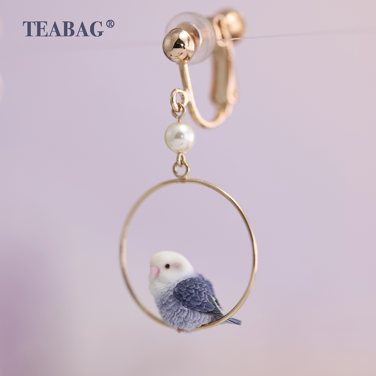 Close-up of one side-facing violet lovebird clip-on earring, with the fitting, clear pad, white bead, hoop and bird fully visible. Sold as a pair.