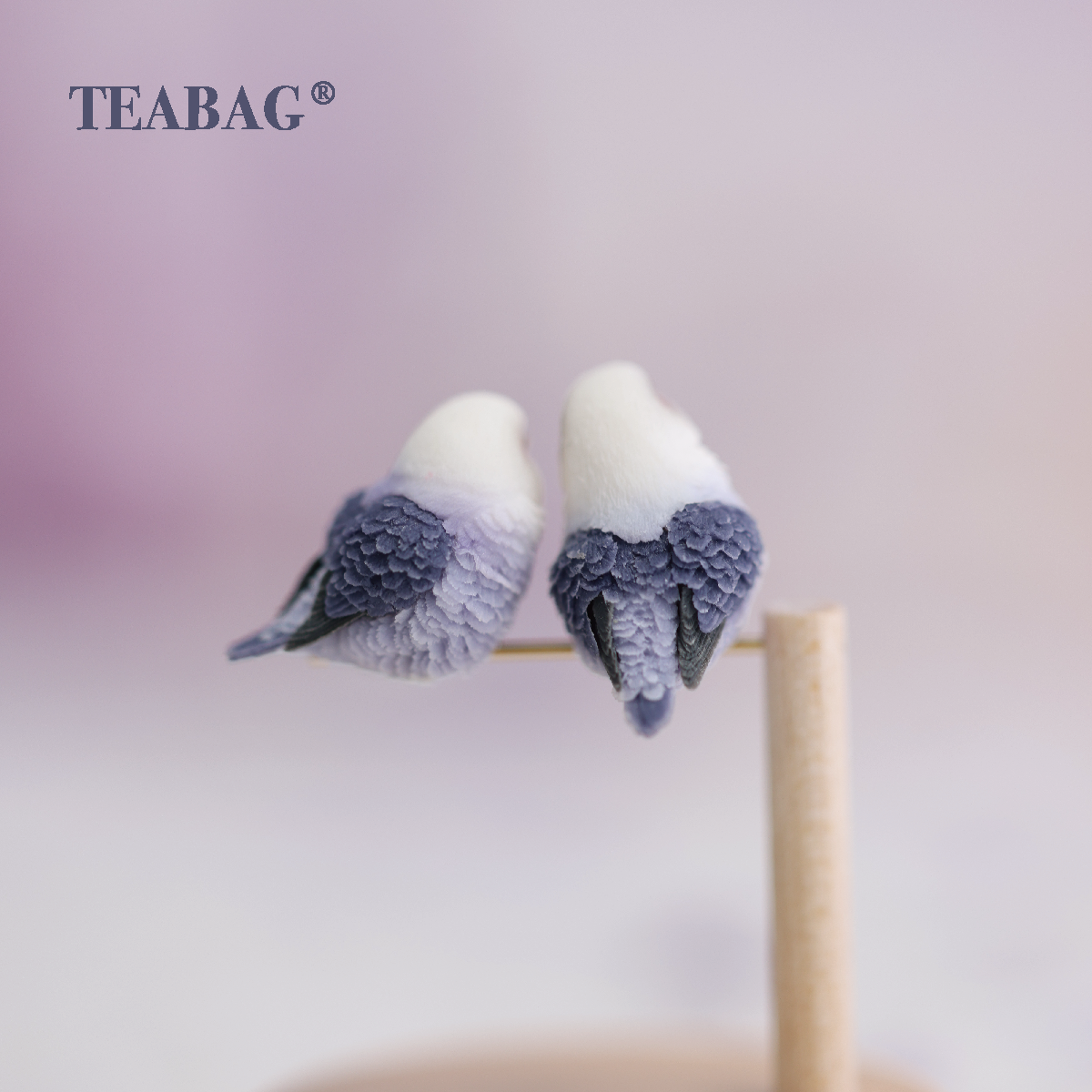 Rear detail of two violet lovebird miniatures on their perch, showing the layered purple wings and tails.