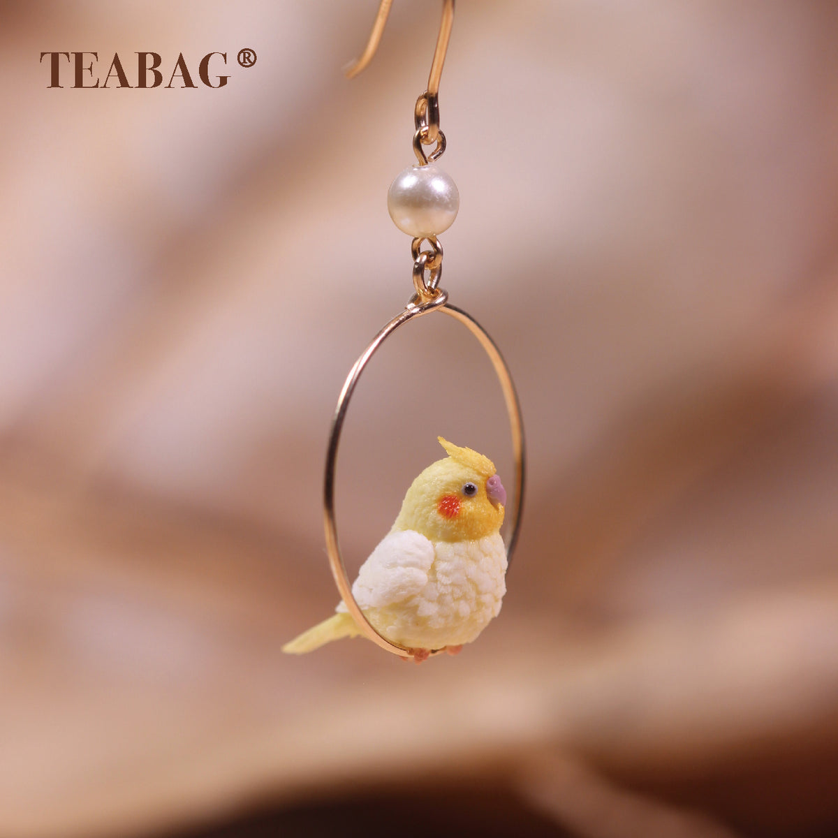 Angled front view of the cockatiel hoop earring and white pearl; the upper hook is partly outside the frame.