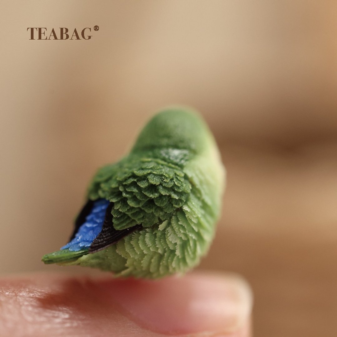 Back of the miniature lovebird, showing sculpted green feathers and a blue tail detail.