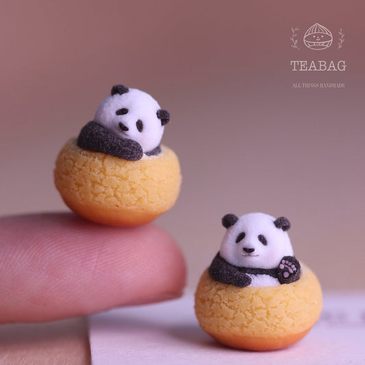 Two miniature panda cream puffs, with one resting on a fingertip for size reference.