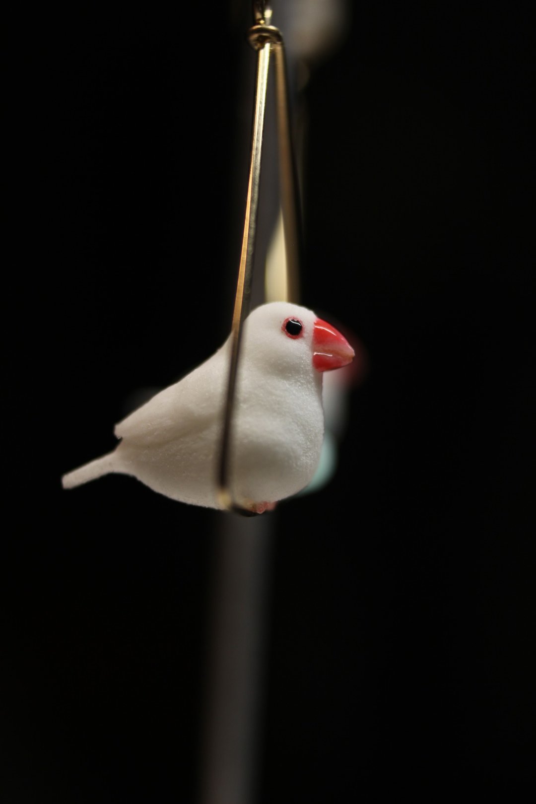 Side view of the Java sparrow charm, showing its red beak and small tail.