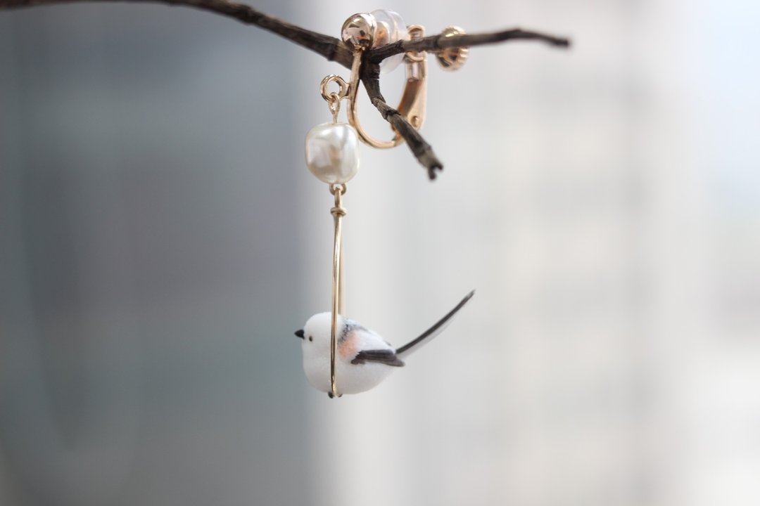 Side profile of the long-tailed tit hoop earring and its dangling white bead.