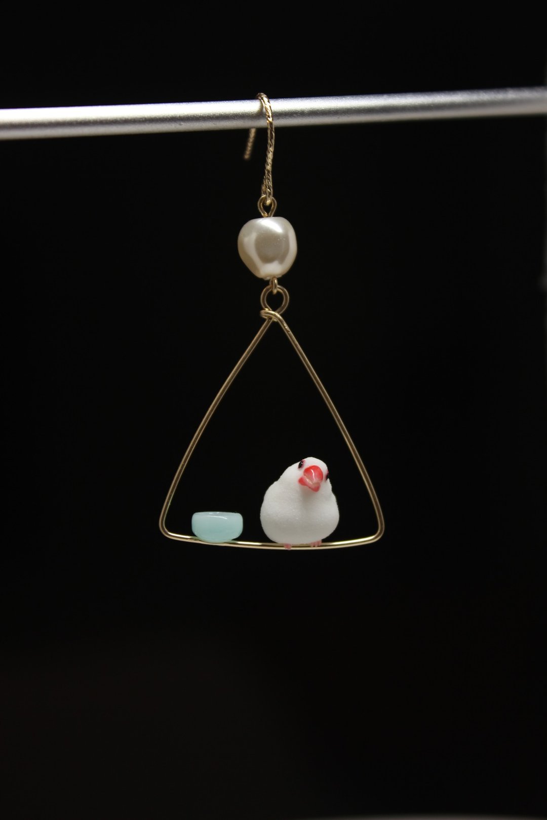Single Java sparrow with a tilted head beside a pale-blue dish on a triangular hoop.