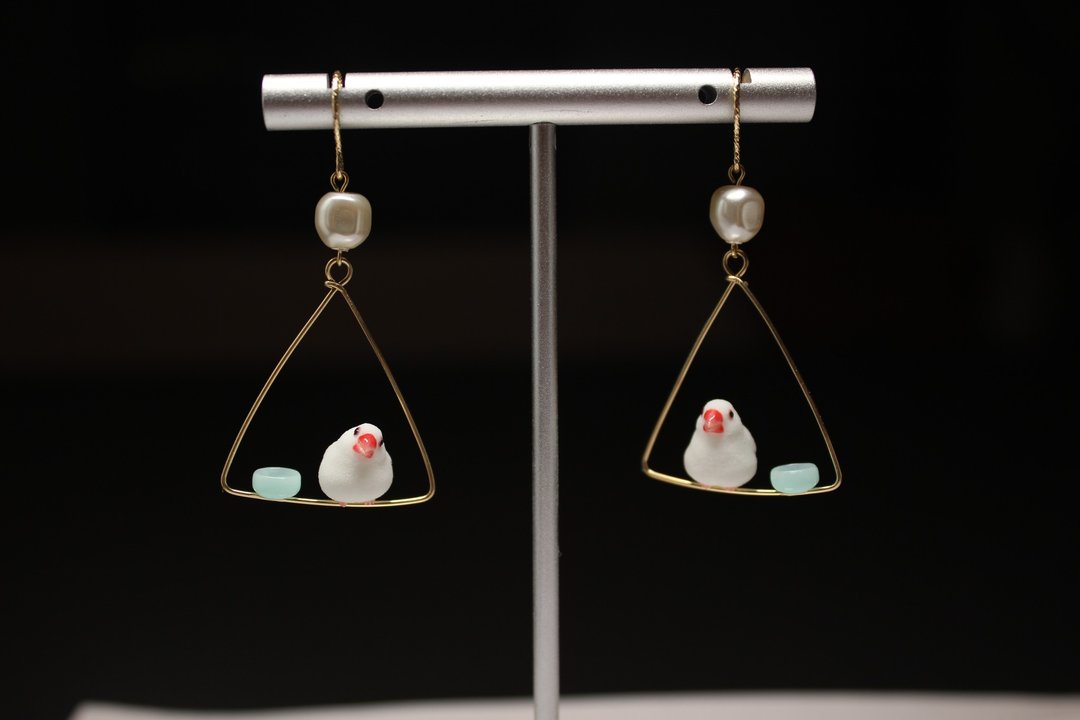Two single-bird Java sparrow earring arrangements displayed on a stand.