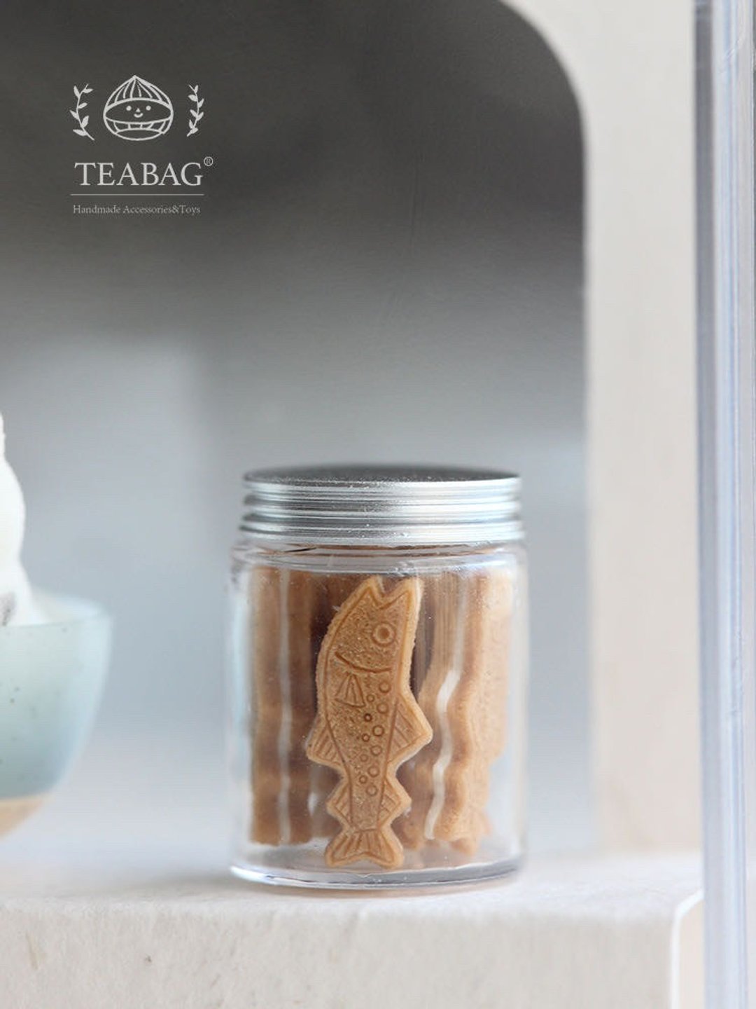 Miniature clear cookie jar with a silver-colored lid and tiny biscuits inside.