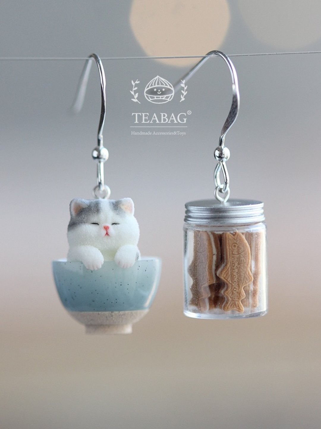 Kitten-in-a-bowl and cookie-jar earrings hanging from silver-colored hooks.