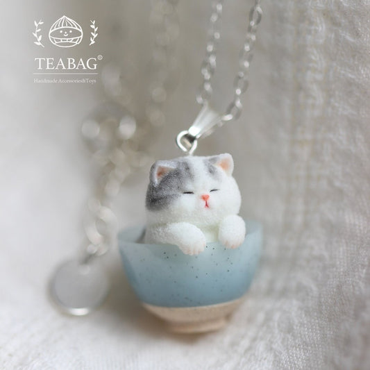 Kitten Bakery necklace with a grey-and-white cat sitting in a blue mixing bowl.