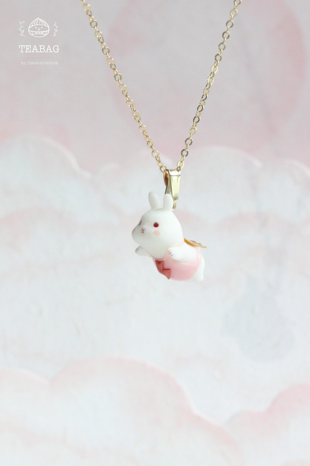 Flying-bunny pendant and chain displayed against a pale pink background.
