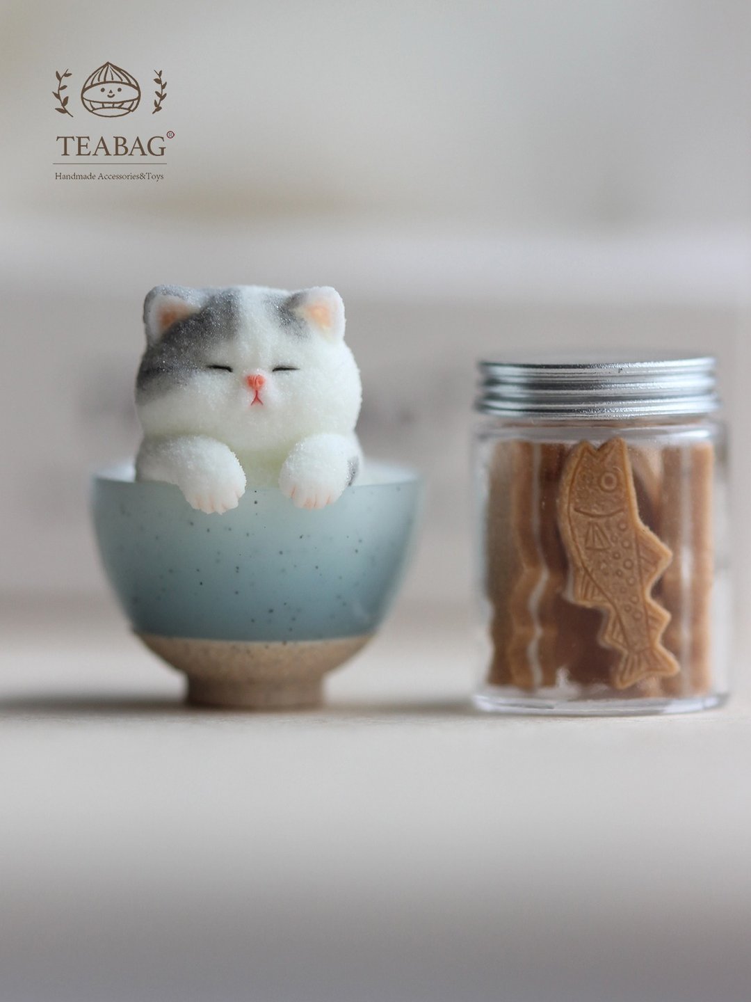 Miniature kitten in a mixing bowl displayed beside a tiny cookie jar.
