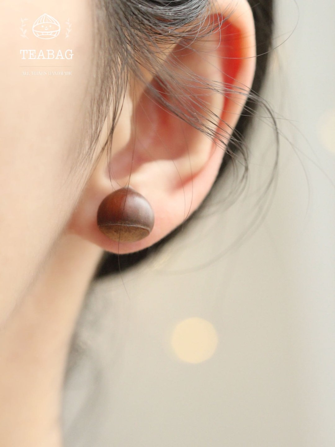 Rear view of a chestnut earring worn on an ear, showing the rounded brown shape.