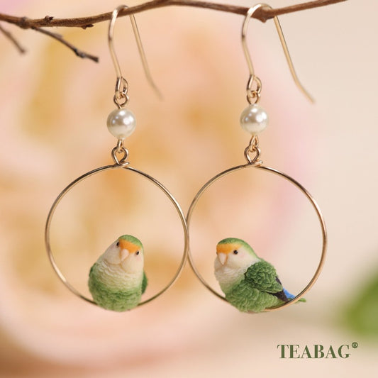 Pair of green lovebird hoop earrings hanging from pierced hooks on a branch.