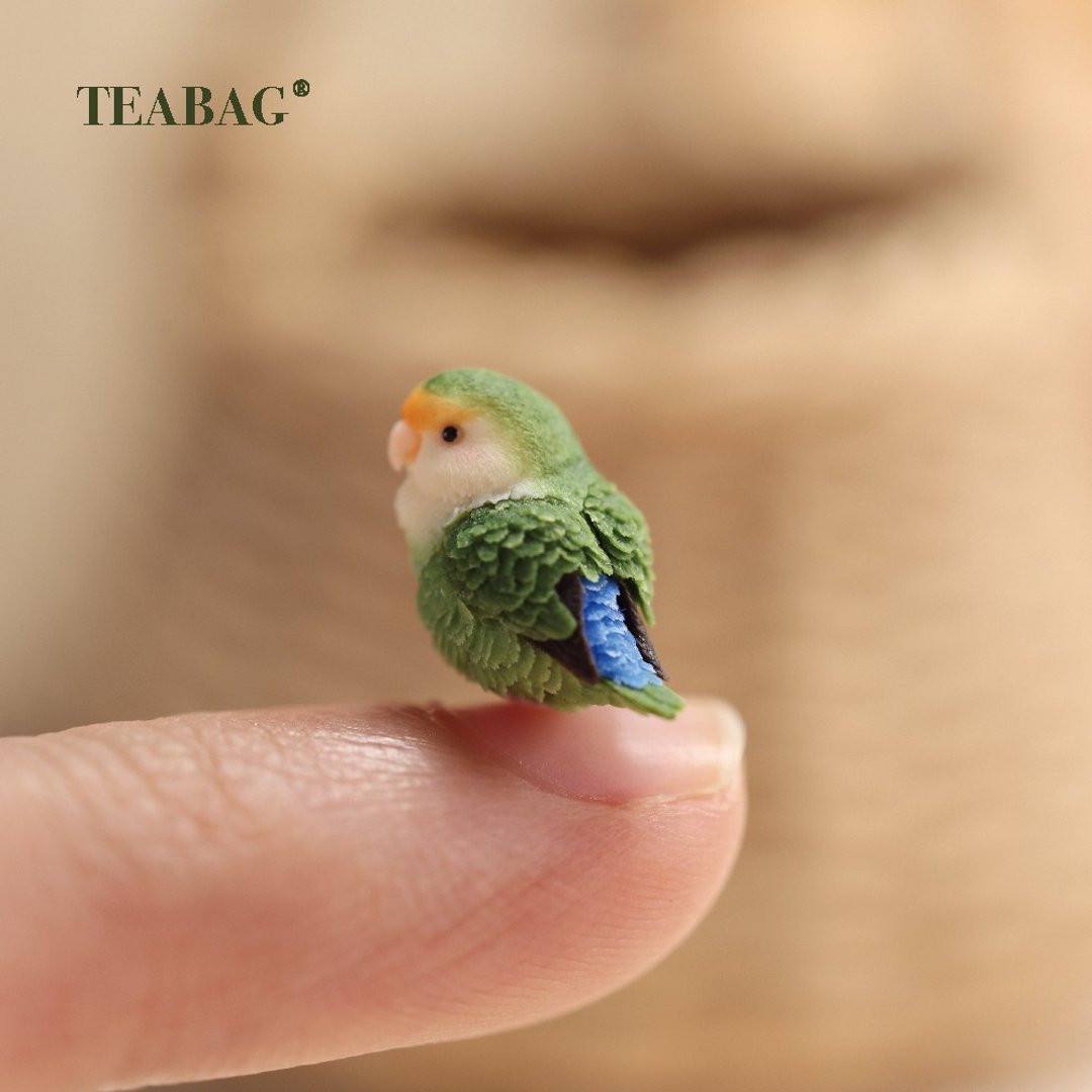 Side view of the tiny lovebird charm, showing its wing and blue tail.