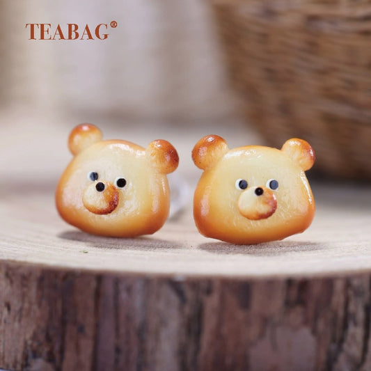 Pair of golden-brown bear bread earrings with smiling faces and rounded ears.