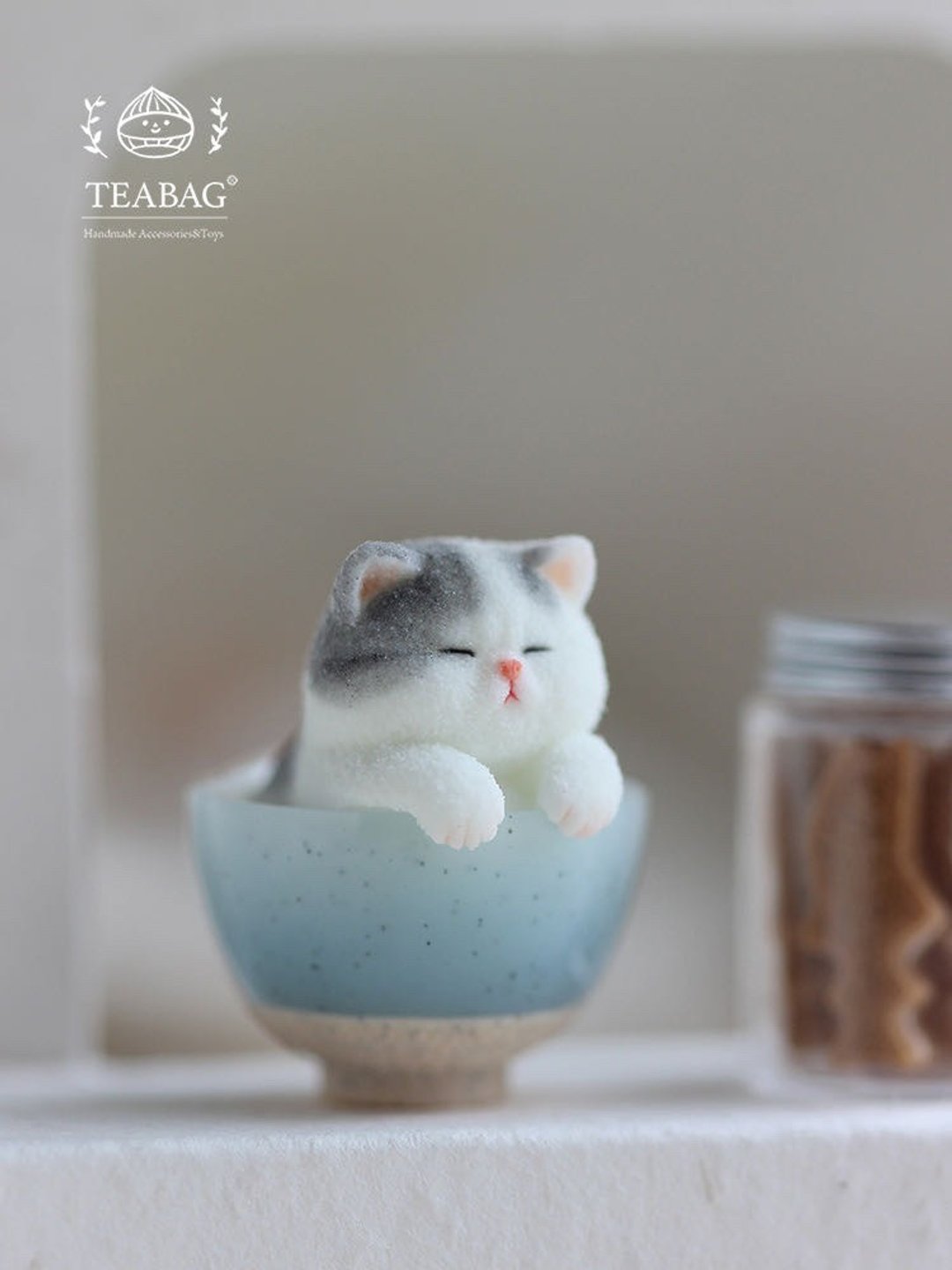 Sleepy kitten charm with white paws resting on the rim of a blue bowl.