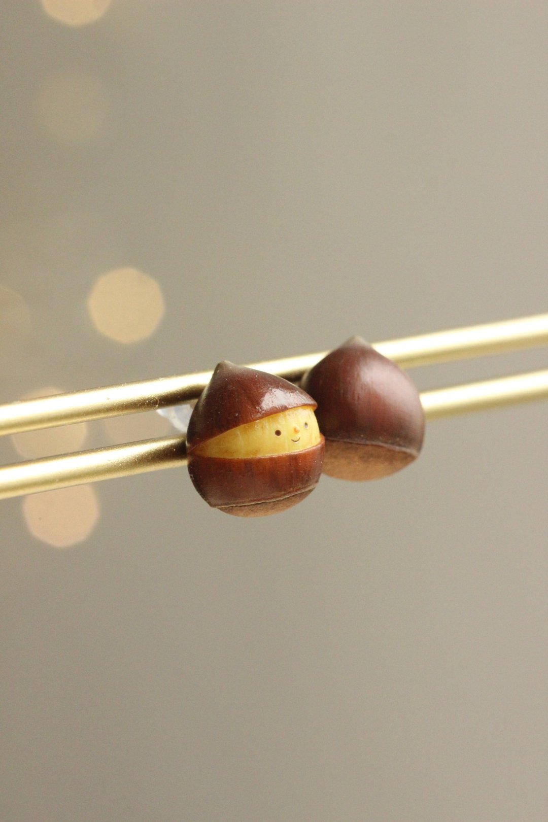 Chestnut earring pair on a display rod, with one smiling face and one brown reverse visible.