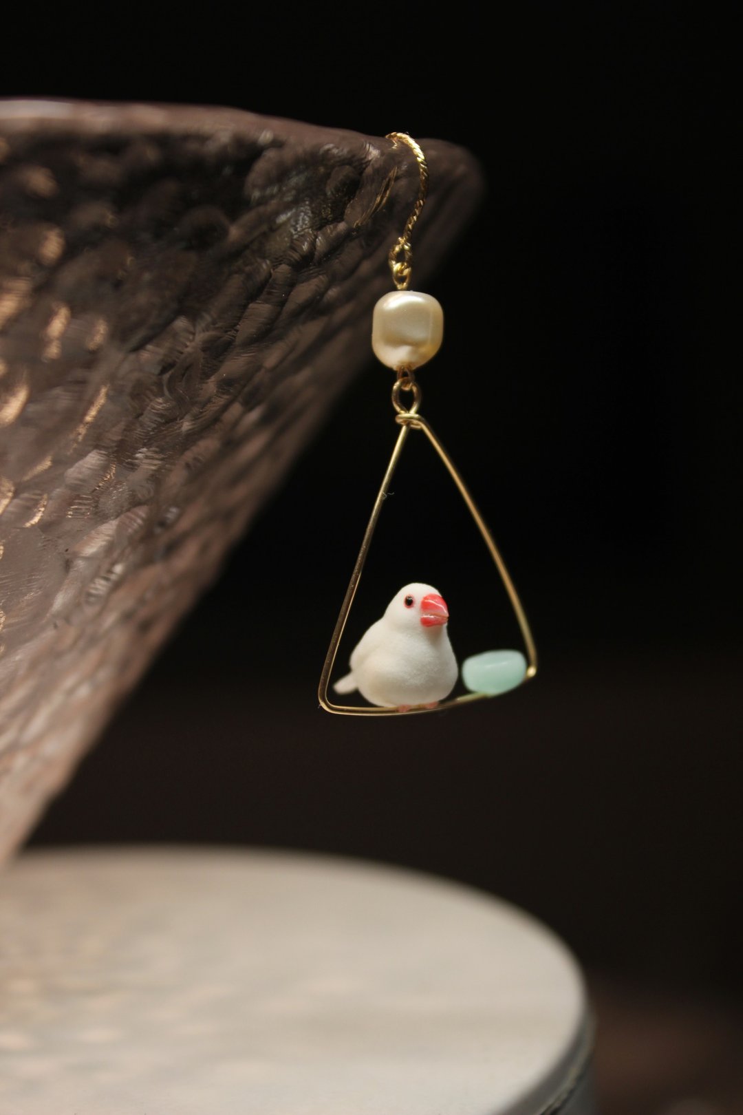 Single-bird Java sparrow earring displayed against a dark branch background.