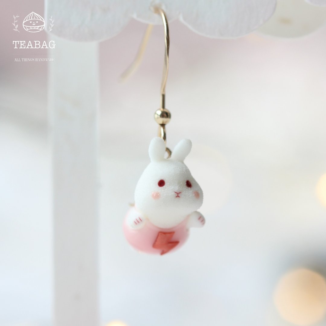 White flying-bunny earring in a pink outfit on a short gold-colored hook.