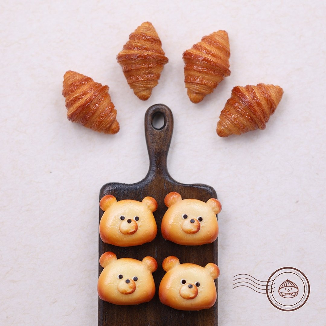 Bakery-themed styling scene with bear bread charms on a small pan and croissant designs nearby.