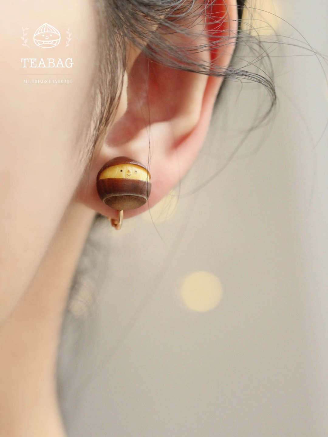 Smiling chestnut earring worn on an ear, showing its tiny face.
