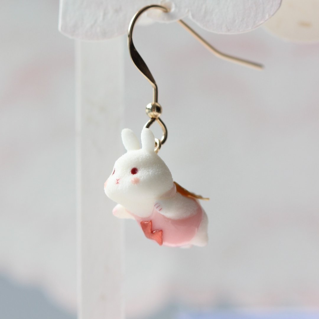 Side view of the miniature white bunny earring, showing its pink outfit and golden cape.