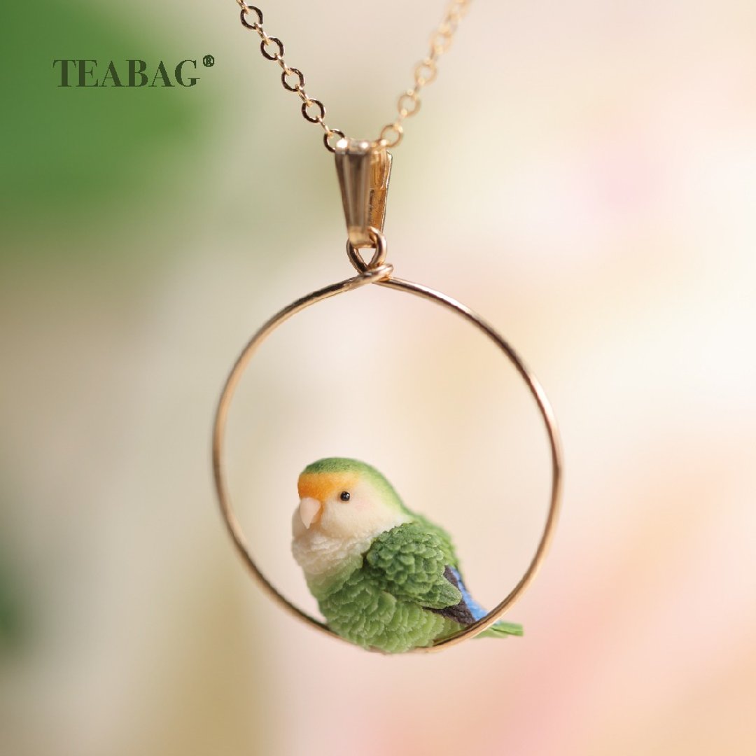 Green lovebird pendant perched at the base of a round hoop on a gold-colored chain.