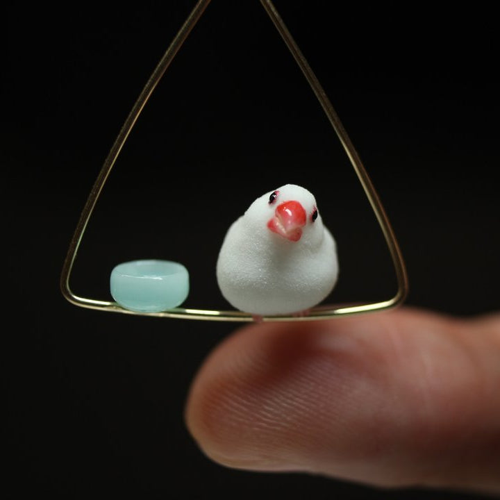 Miniature white Java sparrow and pale-blue dish on a triangular hoop, shown above a fingertip.