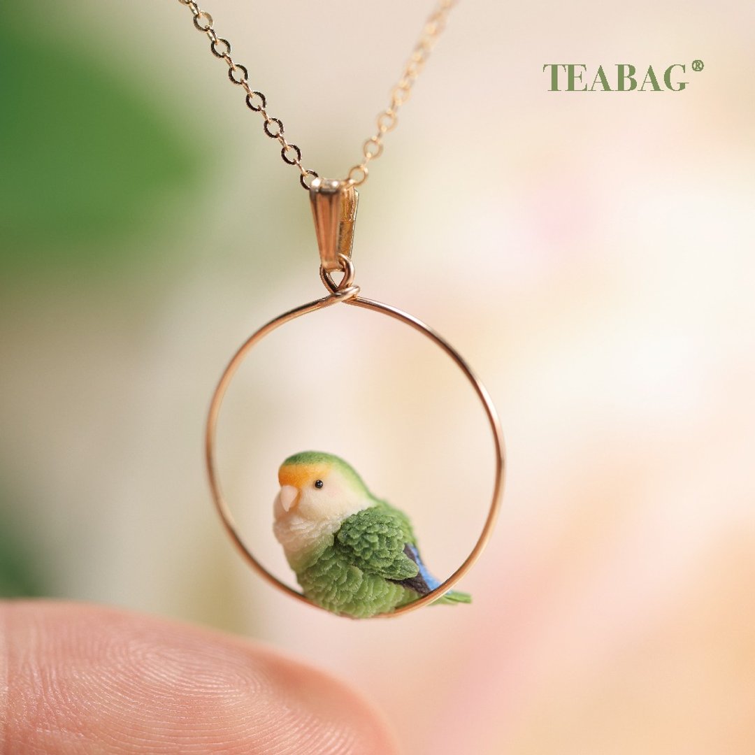 Lovebird hoop pendant shown above a fingertip to illustrate its small size.