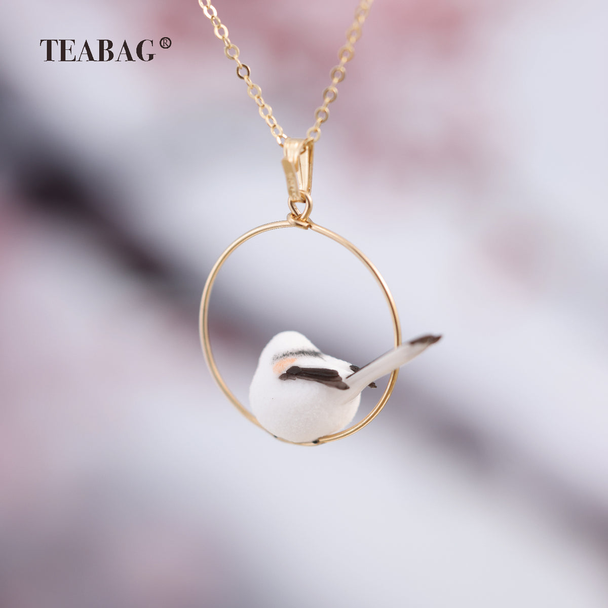 Rear view of the miniature bird pendant, showing its dark wings, long tail and circular hoop.