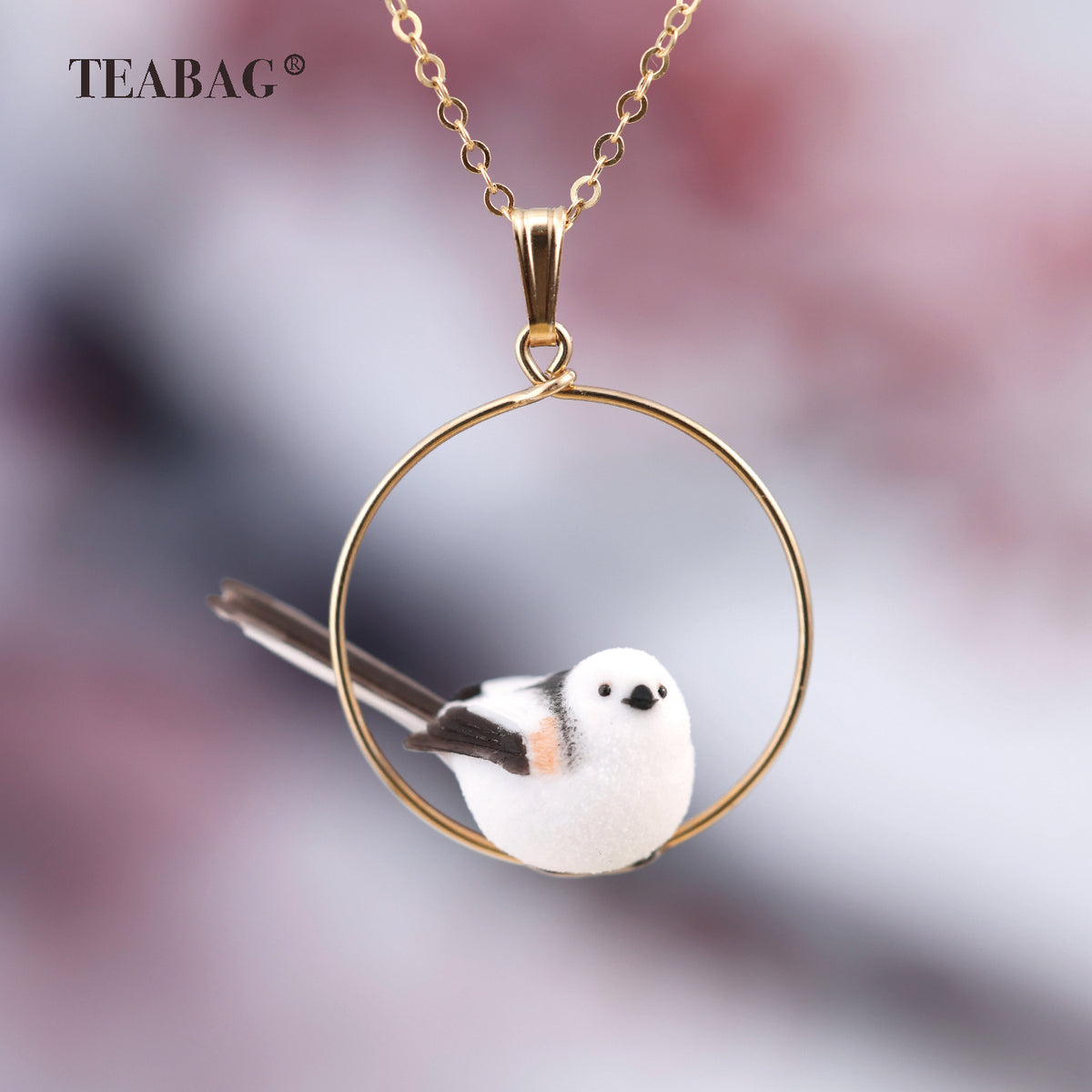 Handmade white bird pendant with dark wings and a long tail, perched inside a gold-tone circular hoop on a chain.