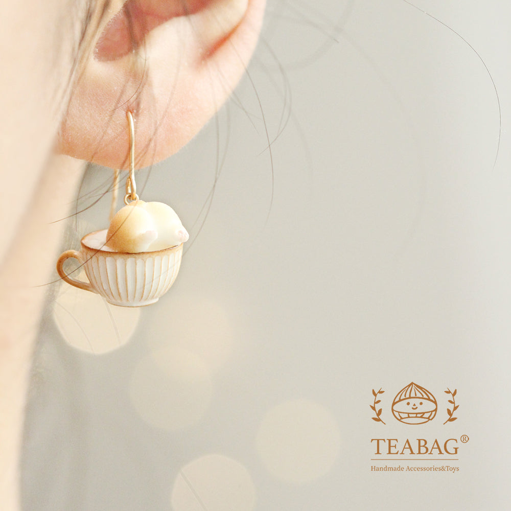 Square photograph of the rear-view Corgi Coffee pierced-hook earring worn on an ear, with the complete hook, cream-and-gold cup and TEABAG logo visible.