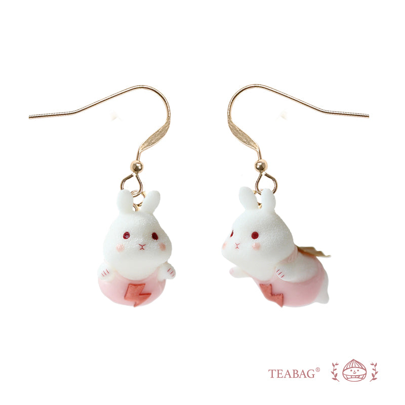 Pair of Flying Bunny earrings with complete short pierced hooks, pink outfits and golden capes on a white background with TEABAG branding.