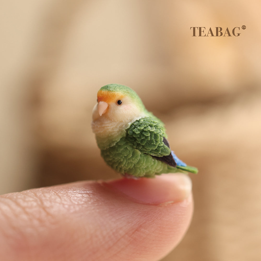 Side-facing green lovebird miniature on a fingertip for scale, showing its pale face, layered green wing feathers and blue tail detail.
