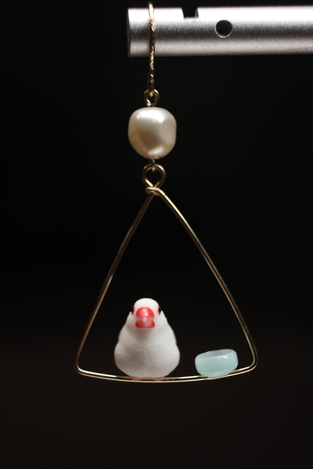 Upright white Java sparrow with a red beak beside a pale blue bowl on a triangular hoop, with the pearl and pierced hook visible. Single earring.