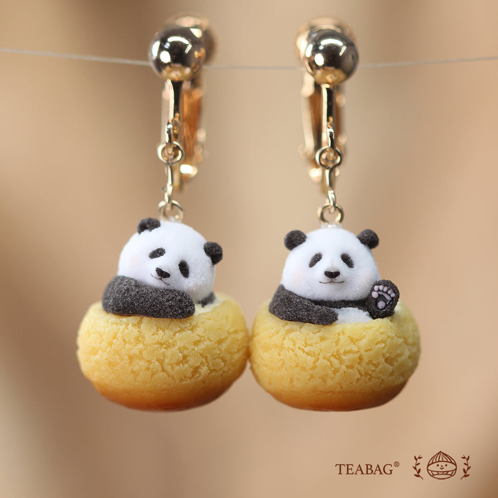Pair of Panda Cream Puff clip-on earrings on a warm brown background, with one waving panda and one tilted-head panda.